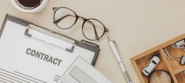 Top view business contract form with coffee eyeglasses car calculator pen with magnifying glass on wooden background.